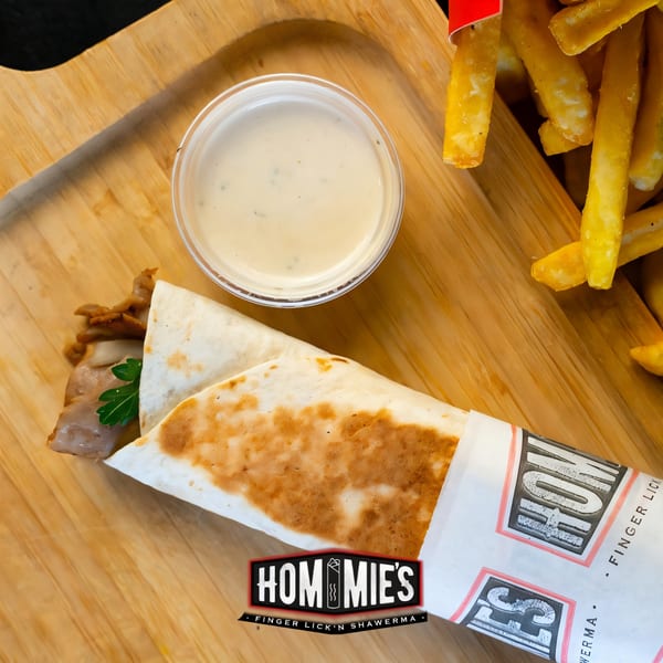 Hommies Shawarma wrap with fries and dipping sauce on a wooden board.