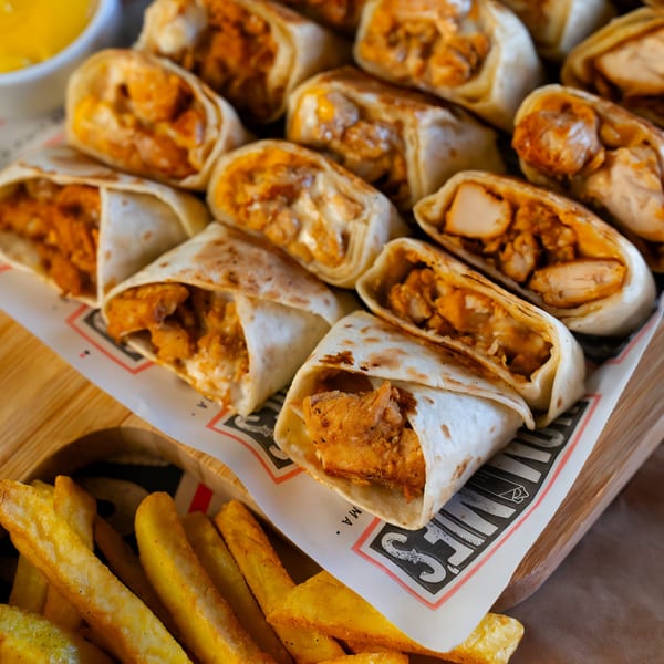 Hommies Shawarma chicken wraps and golden french fries on a wooden board with dipping sauce.